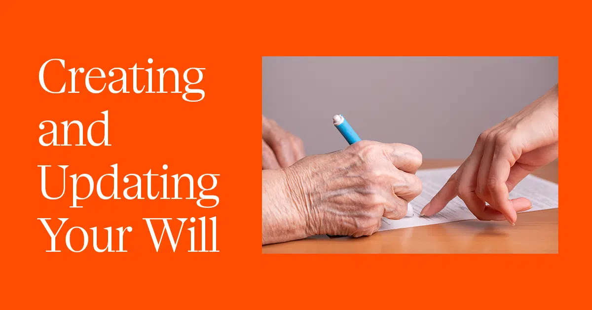 Text reads "Creating and Updating Your Will" on a bright orange background. An image to the right shows close-up of an elderly hand holding a blue pen, poised over a document. Another hand, possibly of a younger person, points at the document, seemingly assisting in the process.