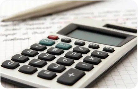 A close-up of a calculator with multiple colored buttons placed on a piece of graph paper with handwritten notes, accompanied by a silver pen.