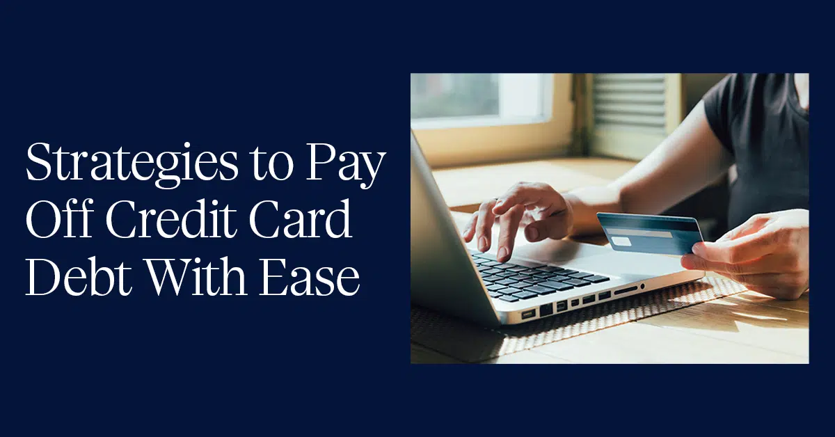 A person holding a credit card in their left hand while using a laptop with their right hand. The text on the left side of the image reads, "Strategies to Pay Off Credit Card Debt With Ease," in white font on a dark blue background. Sunlight streams through a window in the background.
