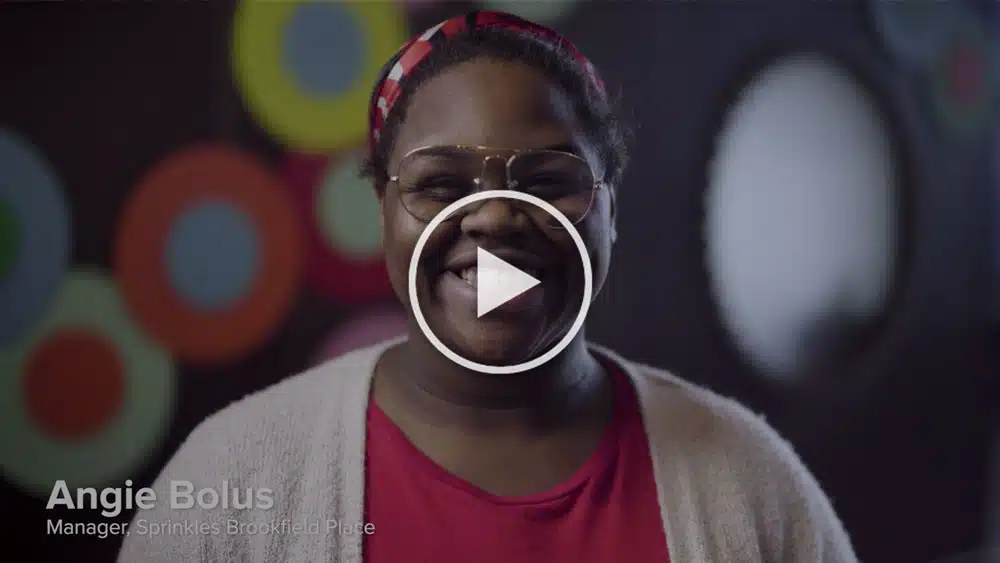 A person wearing glasses and a red shirt with a cardigan smiles at the camera. Text on the image reads, "Angie Bolus Manager Sprinkles Brookfield Place.